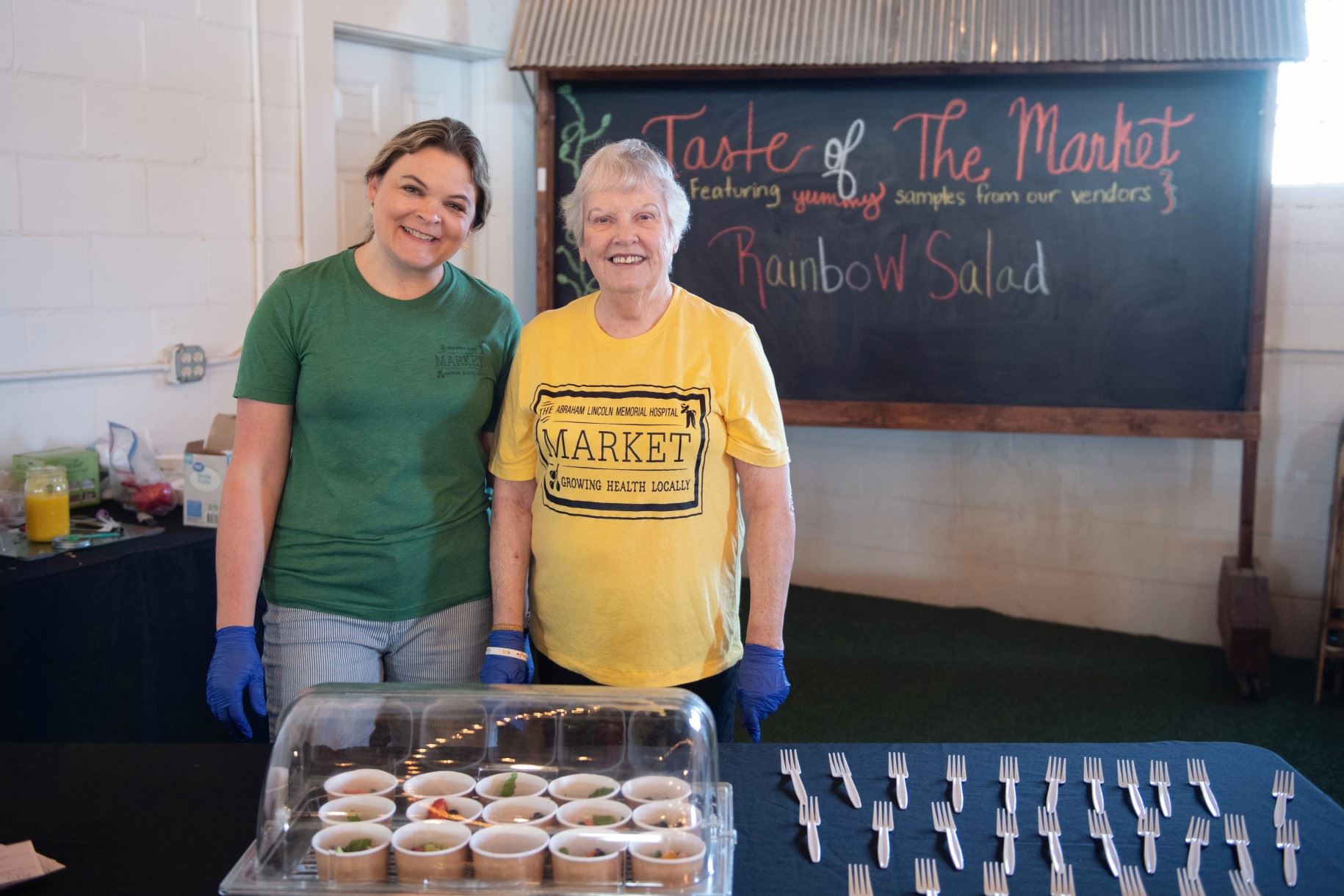 Two women standing next to a table of forks and food